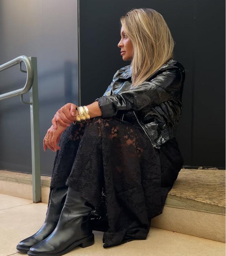 Dona Tata em um look de couro e renda, sentada